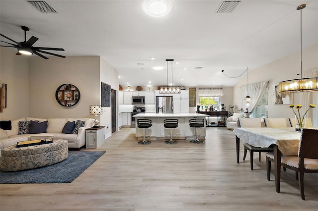 living area featuring recessed lighting, ceiling fan with notable chandelier, visible vents, and light wood finished floors