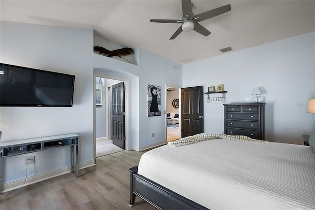 bedroom featuring visible vents, light wood-style flooring, arched walkways, baseboards, and vaulted ceiling