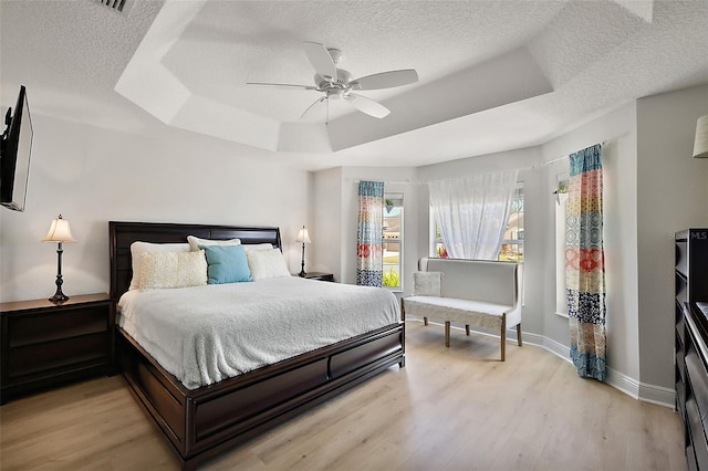 bedroom with a textured ceiling, light wood-type flooring, and a raised ceiling