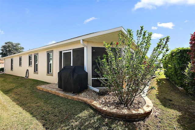 view of side of property featuring stucco siding, a yard, and a sunroom