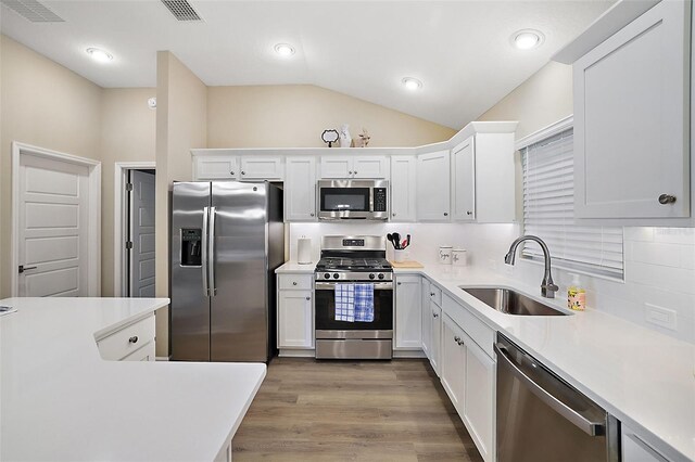 kitchen featuring stainless steel appliances, light countertops, vaulted ceiling, a sink, and wood finished floors