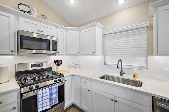 kitchen with a sink, vaulted ceiling, light countertops, appliances with stainless steel finishes, and backsplash