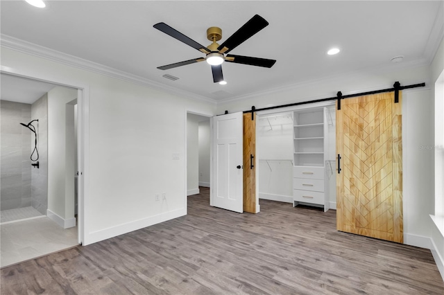 unfurnished bedroom with ornamental molding, a barn door, wood finished floors, and baseboards