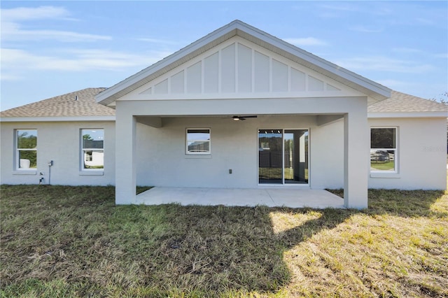 back of property with a patio, a shingled roof, a ceiling fan, a lawn, and board and batten siding