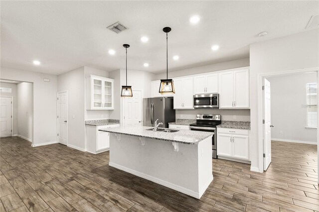 kitchen with an island with sink, appliances with stainless steel finishes, wood finished floors, white cabinets, and a sink