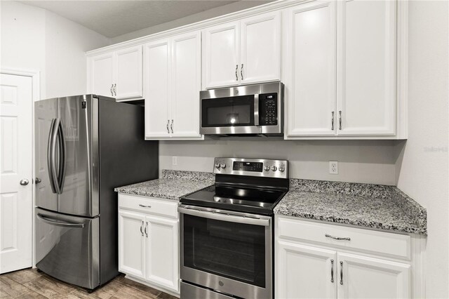 kitchen with white cabinets, light stone countertops, light wood-type flooring, and appliances with stainless steel finishes