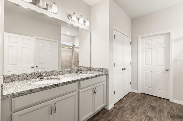 bathroom with double vanity, a stall shower, wood finished floors, and a sink