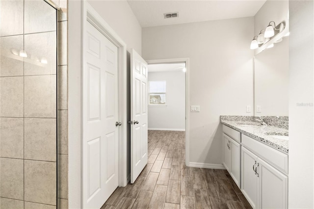 full bath with wood finish floors, visible vents, tiled shower, double vanity, and baseboards