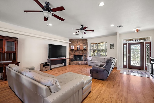 living room with a stone fireplace, light wood-type flooring, visible vents, and recessed lighting