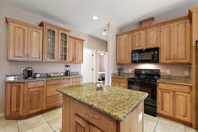 kitchen with light stone counters, light tile patterned floors, glass insert cabinets, a kitchen island, and black appliances