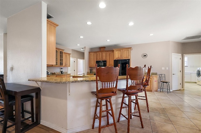 kitchen featuring black microwave, a breakfast bar area, stone counters, fridge, and washer / clothes dryer