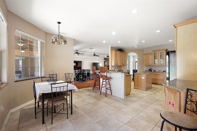 kitchen with arched walkways, a breakfast bar area, light brown cabinetry, freestanding refrigerator, and light tile patterned flooring