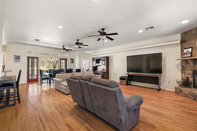 living area with a stone fireplace, light wood-type flooring, visible vents, and recessed lighting