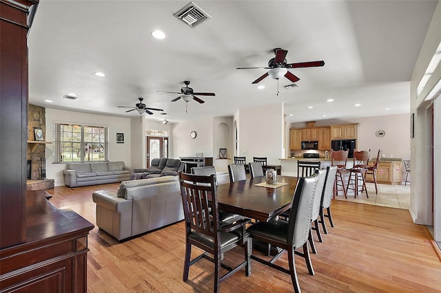 dining room featuring light wood finished floors, recessed lighting, visible vents, and a stone fireplace