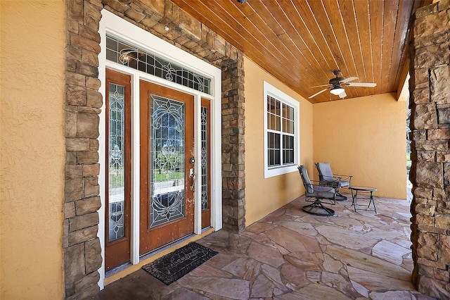 property entrance featuring stone siding, a porch, a ceiling fan, and stucco siding