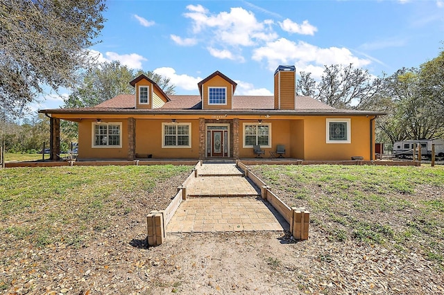 view of front of house with a chimney, a front lawn, and stucco siding