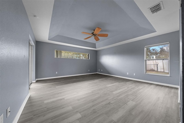 unfurnished room featuring a tray ceiling, wood finished floors, baseboards, and visible vents