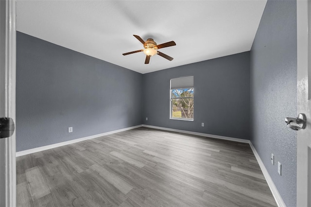 spare room featuring a ceiling fan, wood finished floors, baseboards, and a textured wall