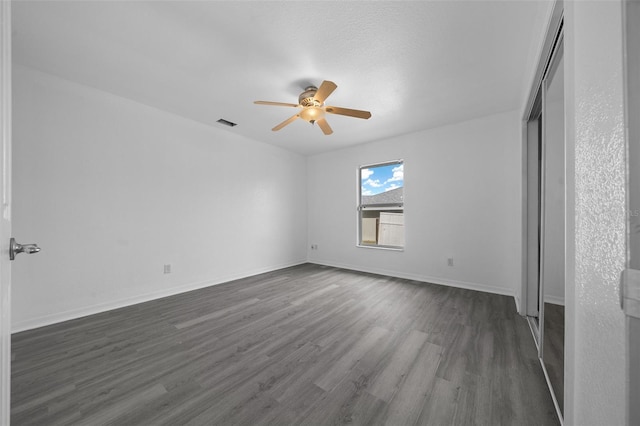 unfurnished bedroom featuring dark wood-style floors, visible vents, baseboards, ceiling fan, and a closet