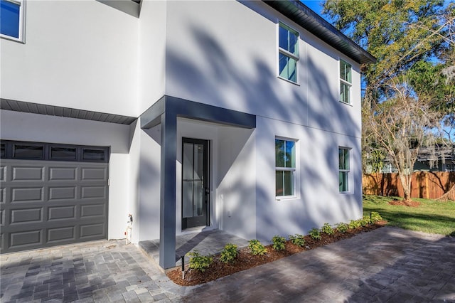 doorway to property featuring a garage, fence, and stucco siding