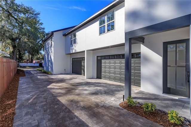 view of side of property featuring decorative driveway, an attached garage, fence, and stucco siding