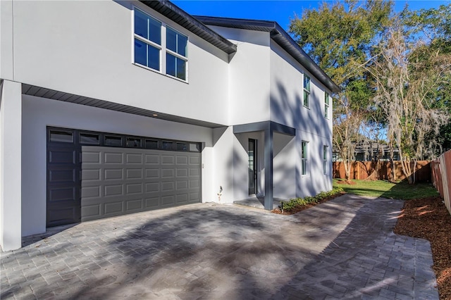 view of property exterior with decorative driveway, an attached garage, fence, and stucco siding