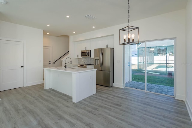 kitchen with white cabinets, decorative backsplash, light wood-style flooring, stainless steel appliances, and a sink