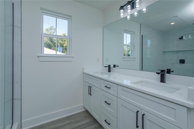 bathroom featuring double vanity, a sink, a marble finish shower, and baseboards