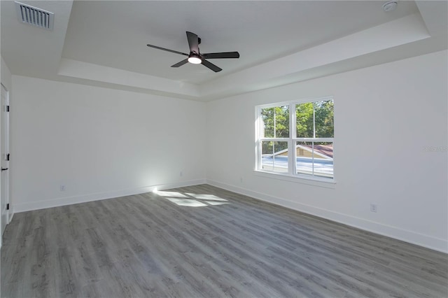 empty room with wood finished floors, a raised ceiling, visible vents, and baseboards