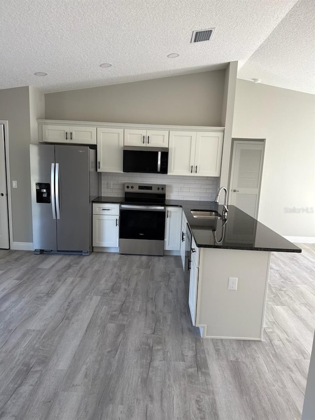 kitchen with visible vents, dark countertops, appliances with stainless steel finishes, vaulted ceiling, and a sink