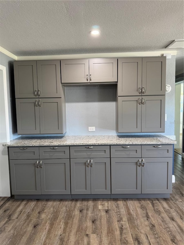 kitchen with light stone counters, a textured ceiling, gray cabinetry, and wood finished floors