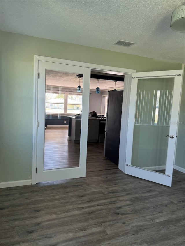 hall with dark wood-style floors, a textured ceiling, visible vents, and baseboards