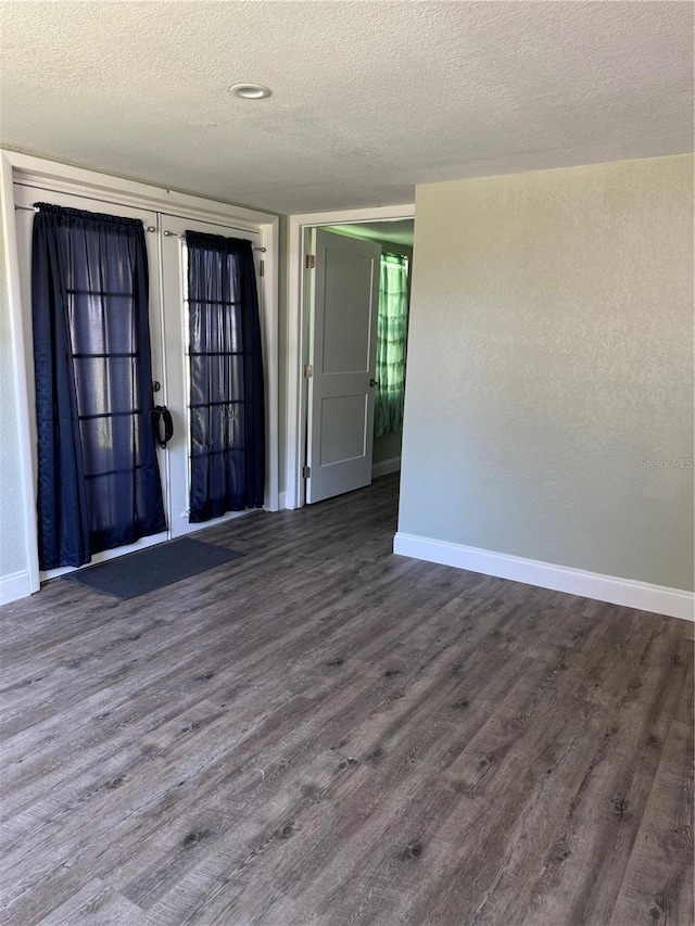 spare room featuring baseboards, dark wood finished floors, and a textured ceiling