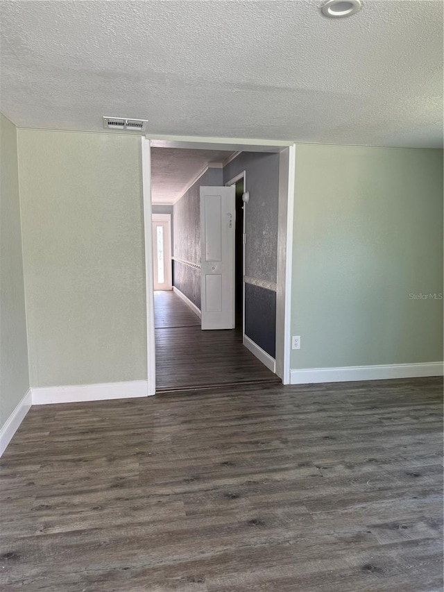 unfurnished room with baseboards, visible vents, a textured wall, dark wood-type flooring, and a textured ceiling