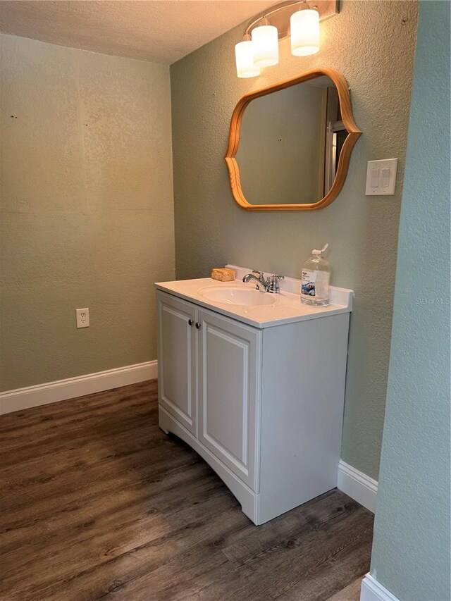 bathroom featuring a textured wall, baseboards, wood finished floors, and vanity