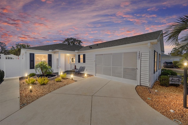 single story home with a garage, concrete driveway, a shingled roof, and fence