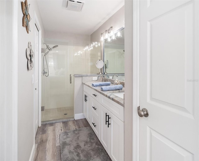 full bath featuring double vanity, a stall shower, wood finished floors, and visible vents