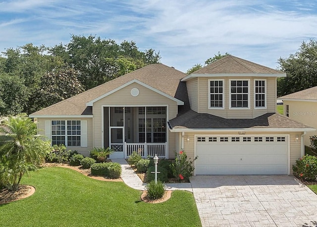 view of front of property featuring an attached garage, a sunroom, roof with shingles, decorative driveway, and a front yard