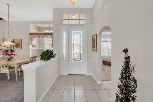 foyer entrance featuring light carpet, baseboards, arched walkways, a chandelier, and light tile patterned flooring