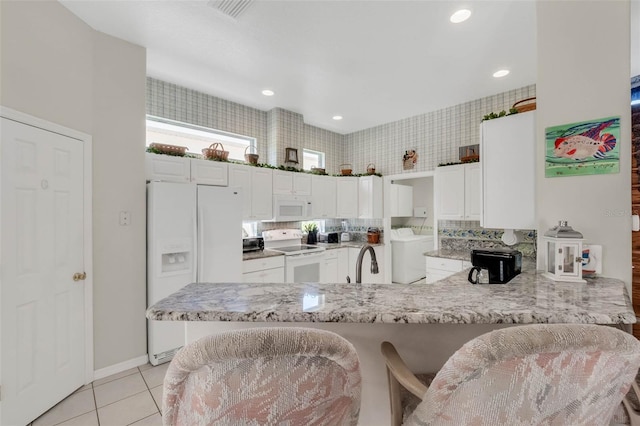 kitchen featuring light tile patterned flooring, a peninsula, white appliances, a sink, and white cabinets