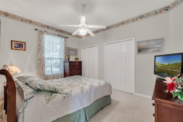 bedroom featuring light colored carpet, ceiling fan, baseboards, and two closets