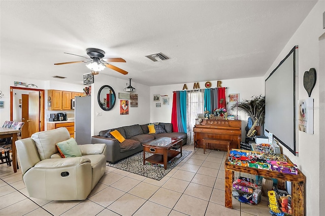 living area featuring light tile patterned floors, a ceiling fan, visible vents, and a textured ceiling