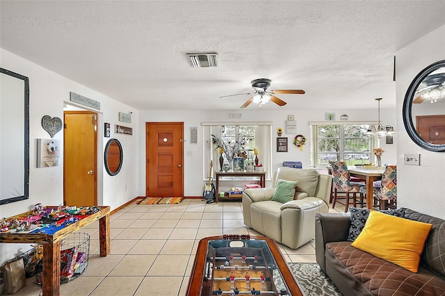 living room featuring visible vents, ceiling fan with notable chandelier, a textured ceiling, light tile patterned flooring, and baseboards