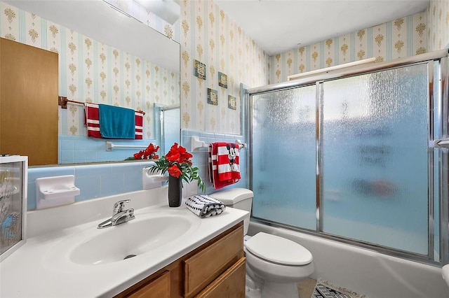 bathroom featuring wallpapered walls, a wainscoted wall, toilet, combined bath / shower with glass door, and vanity