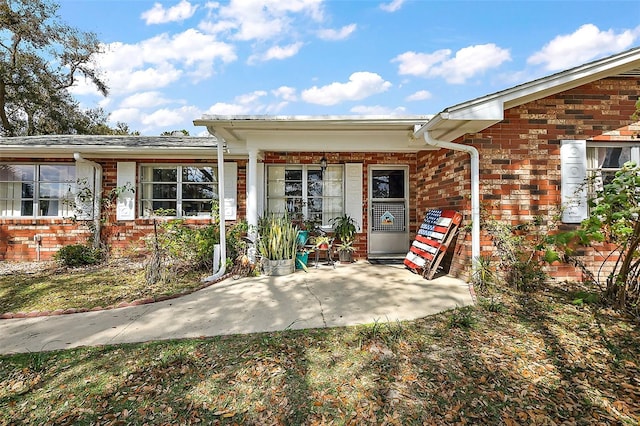 view of exterior entry with a patio area and brick siding