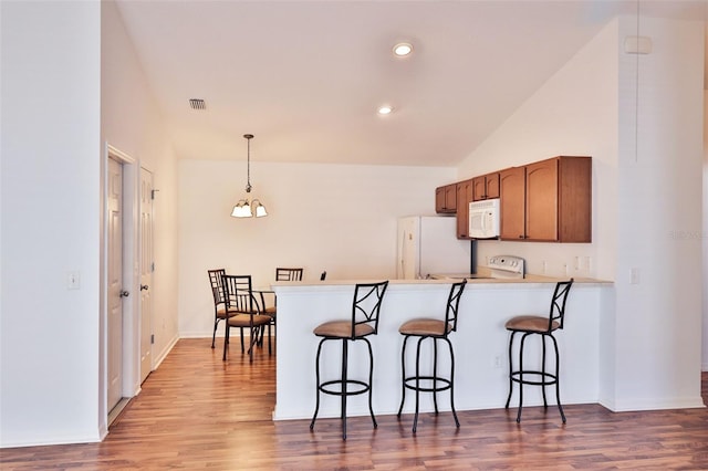 kitchen featuring white appliances, visible vents, light wood-style flooring, a peninsula, and a kitchen bar