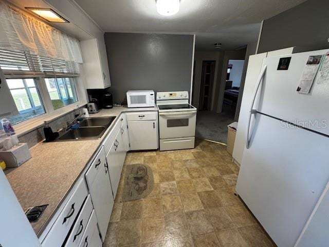 kitchen with white appliances, a sink, light countertops, white cabinets, and stone finish flooring