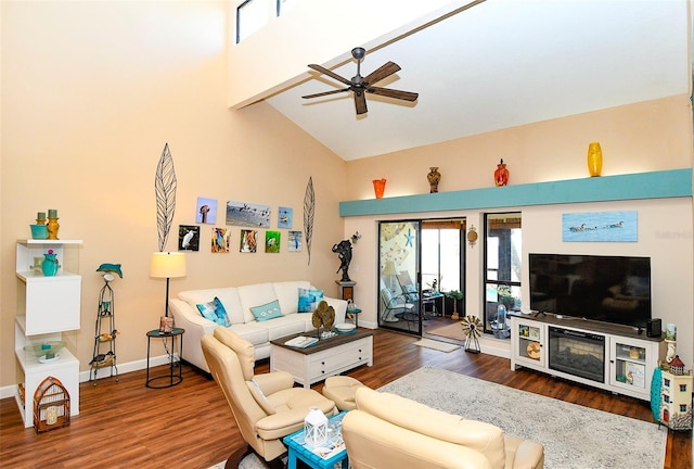 living room featuring a ceiling fan, wood finished floors, baseboards, and a towering ceiling