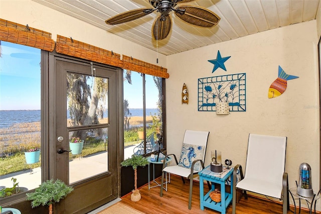 sitting room featuring a ceiling fan, wood finished floors, a water view, wooden ceiling, and a textured wall