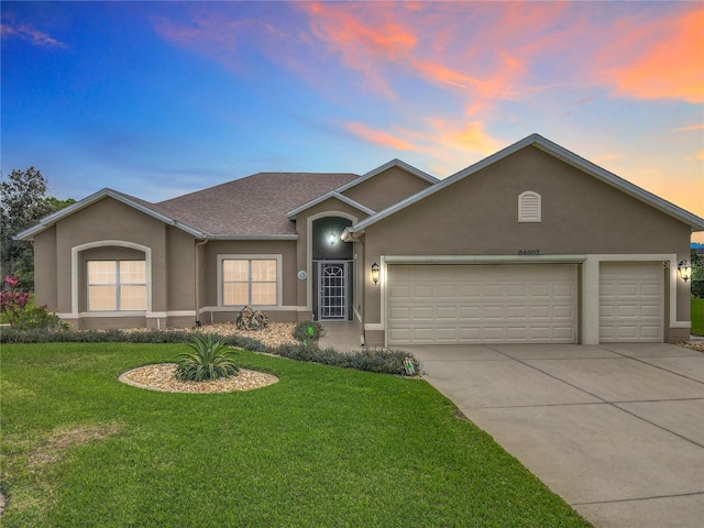 ranch-style house featuring roof with shingles, stucco siding, an attached garage, a front yard, and driveway